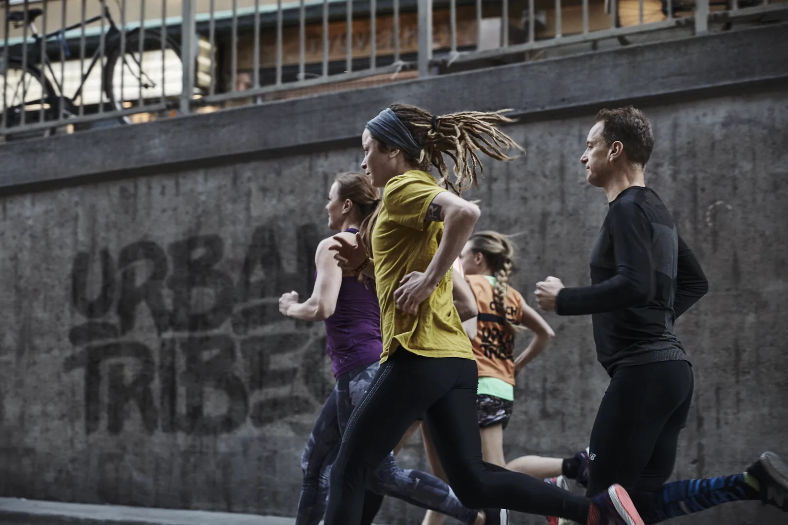 En löpgrupp springer förbi en betongvägg med texten Urban Tribes sprejad i stort
