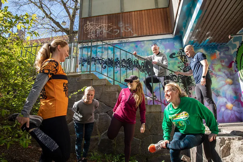 En löpgrupp i färgglada tröjor gör övningar vid en graffitivägg