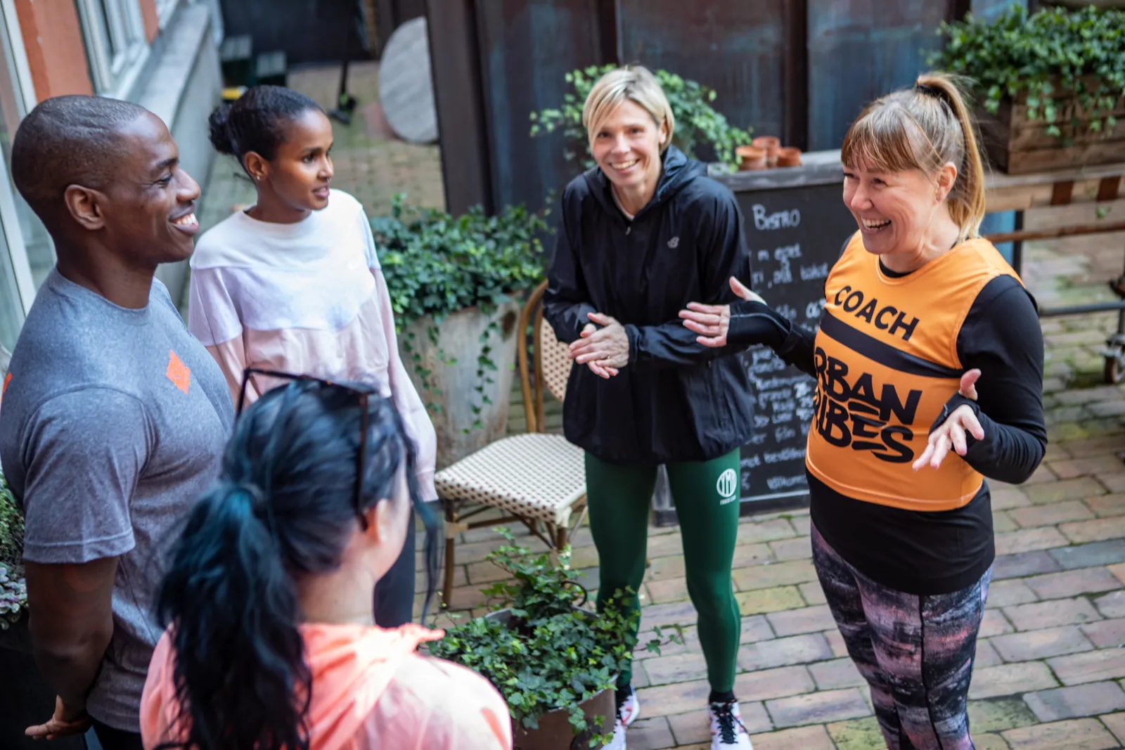 Lisa McRae i orange Urban Tribes-tröja pratar med deltagare framför en graffitivägg