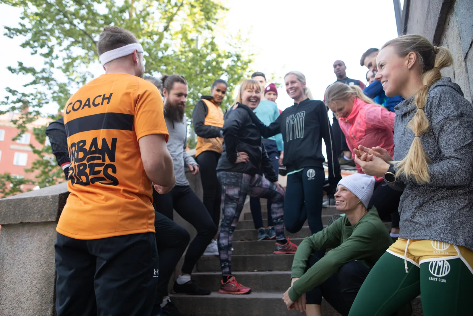 En hel grupp kollegor tränar i en trappa utomhus tillsammans med en coach i orange tröja