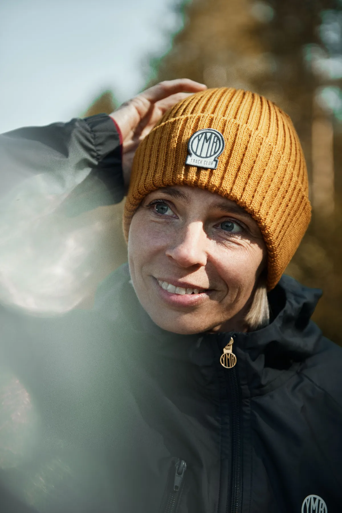 En deltagare i orange mössa ler i vintersolen